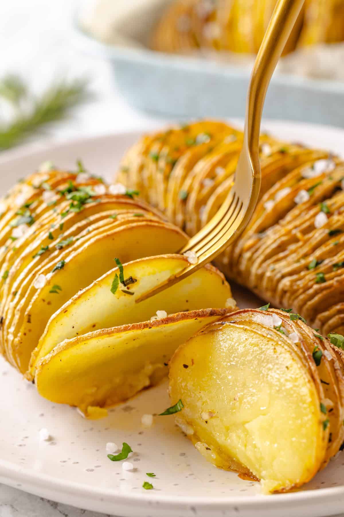 Hasselback potatoes are perfect for a party! The edges get crispy, the insides are tender, and garlic herb butter makes them irresistible. Fork picking up slice of hasselback potatoes.