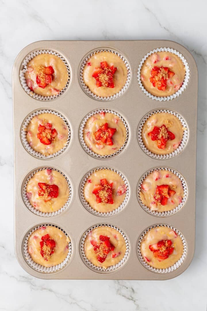 These Vegan Strawberry Muffins are top-notch. Tender, fluffy, and loaded with fresh fruit, they're the perfect way to start the day. Muffin cups filled 3/4 full with strawberry muffin batter and topped with fresh strawberries and coarse sugar.