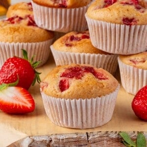 Strawberry muffins piled on a wooden surface.
