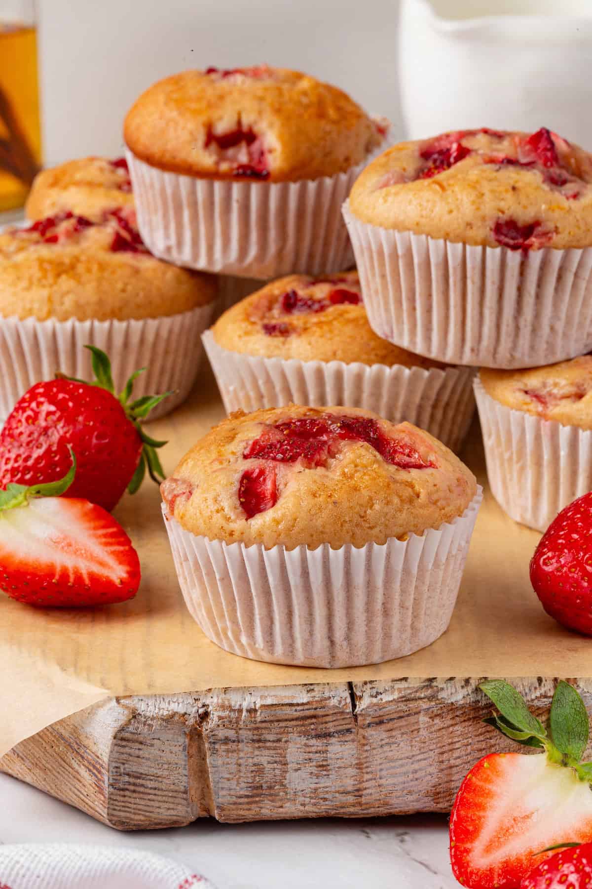 These Vegan Strawberry Muffins are top-notch. Tender, fluffy, and loaded with fresh fruit, they're the perfect way to start the day. Strawberry muffins piled on a wooden surface.