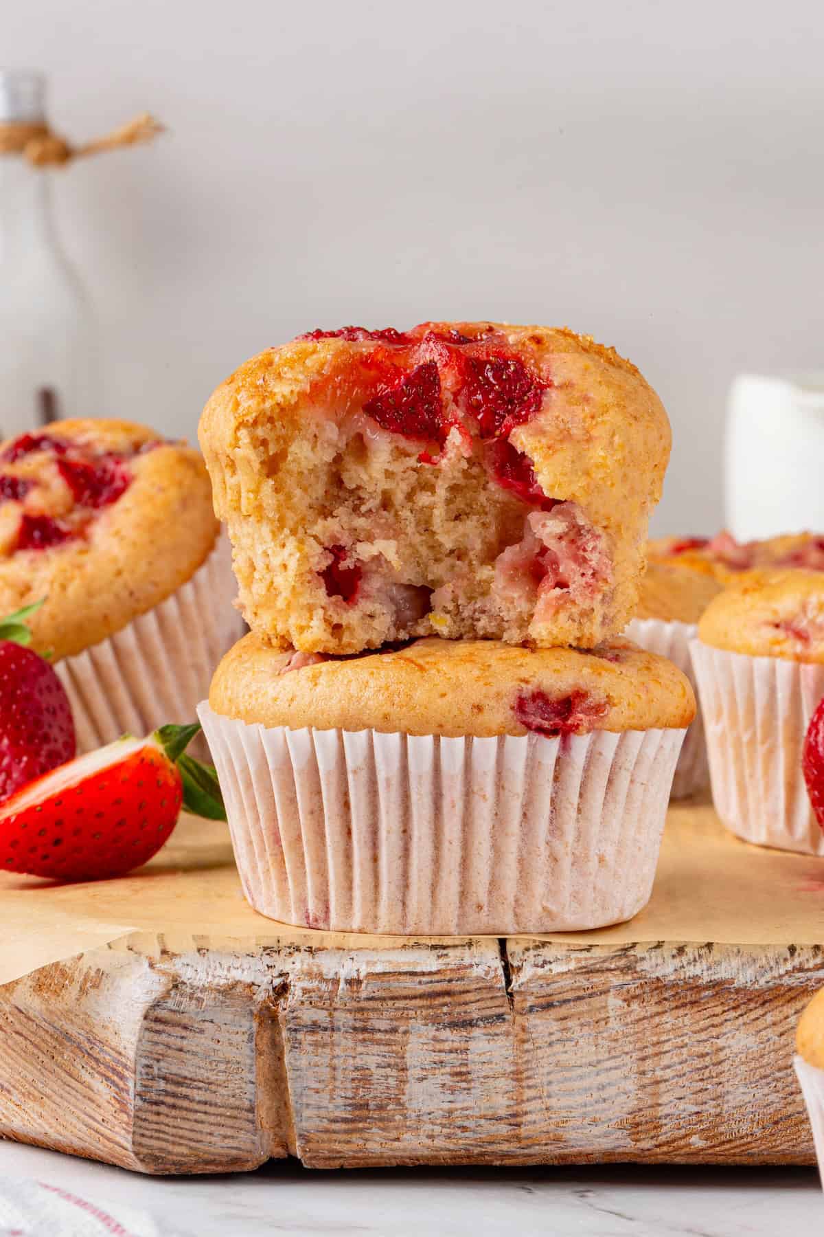 These Vegan Strawberry Muffins are top-notch. Tender, fluffy, and loaded with fresh fruit, they're the perfect way to start the day. A strawberry muffin with a bite taken out of it sitting on top of another strawberry muffin.
