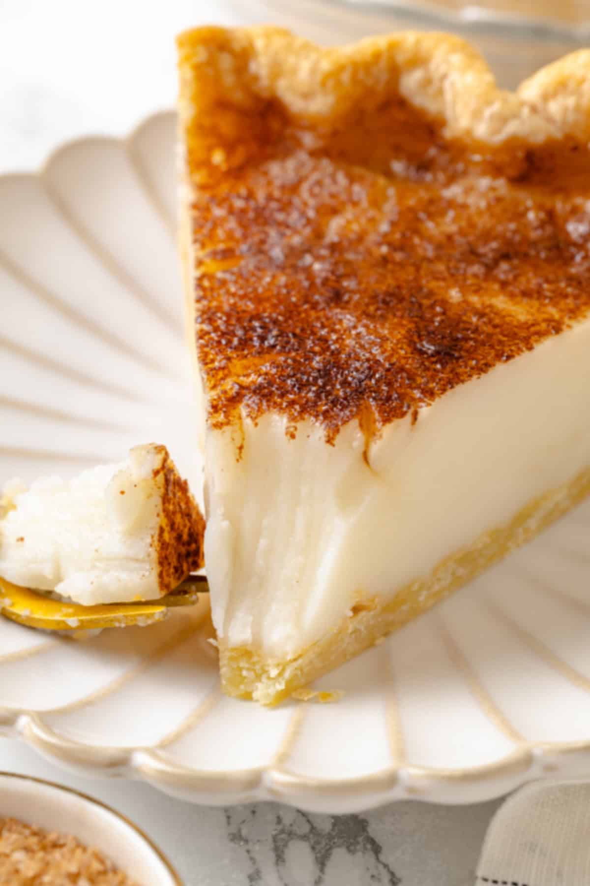 Slice of sugar cream pie on plate with tip on fork.