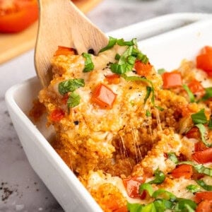 A wooden spatula diving into quinoa casserole.