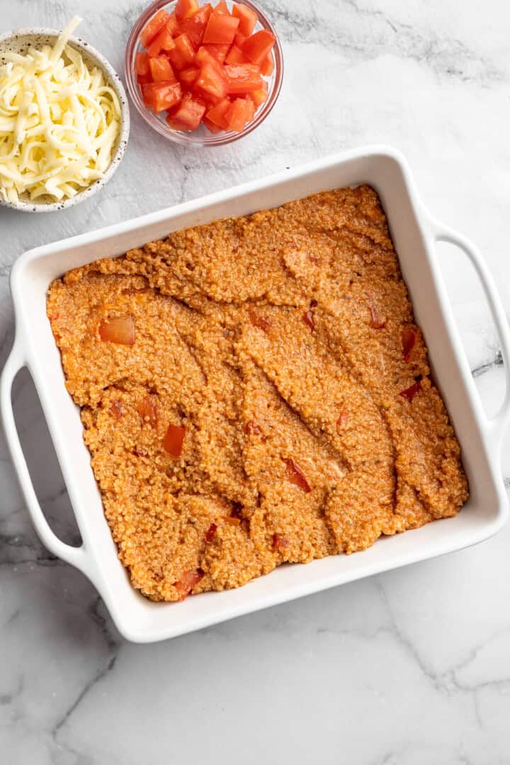 Spreading the filling for cheesy quinoa casserole into a baking dish.