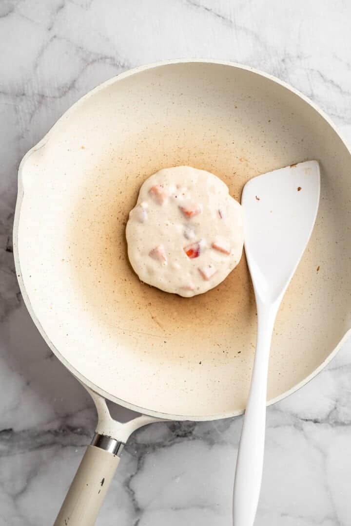 These strawberry pancakes are incredibly fluffy and jam-packed with fresh strawberries. Plus, they're gluten-free and vegan! Cooking a pancake on a pan (side one)