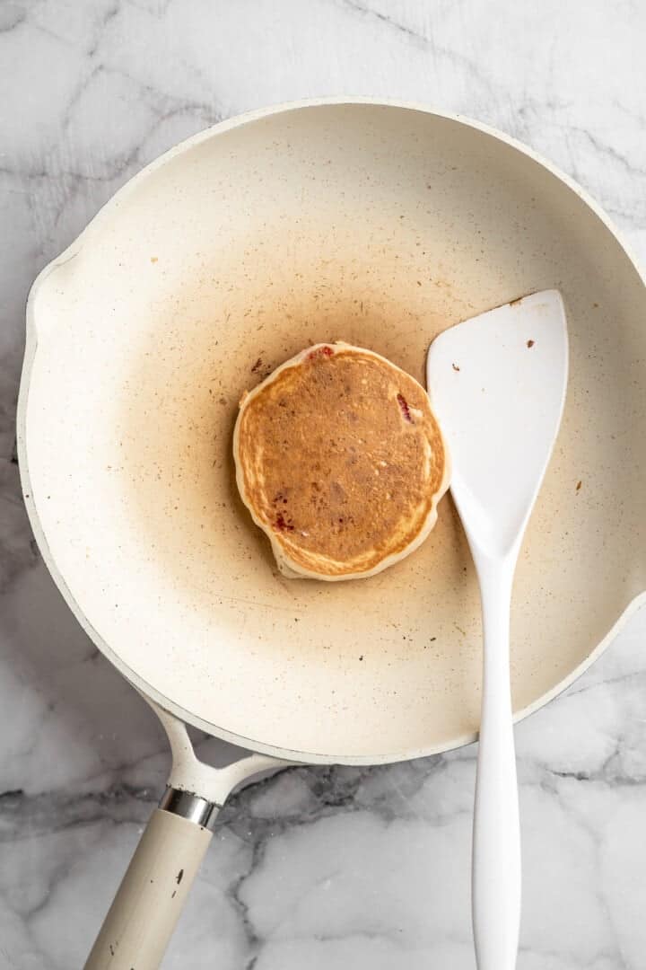 These strawberry pancakes are incredibly fluffy and jam-packed with fresh strawberries. Plus, they're gluten-free and vegan! Cooking a pancake on a pan (side two).