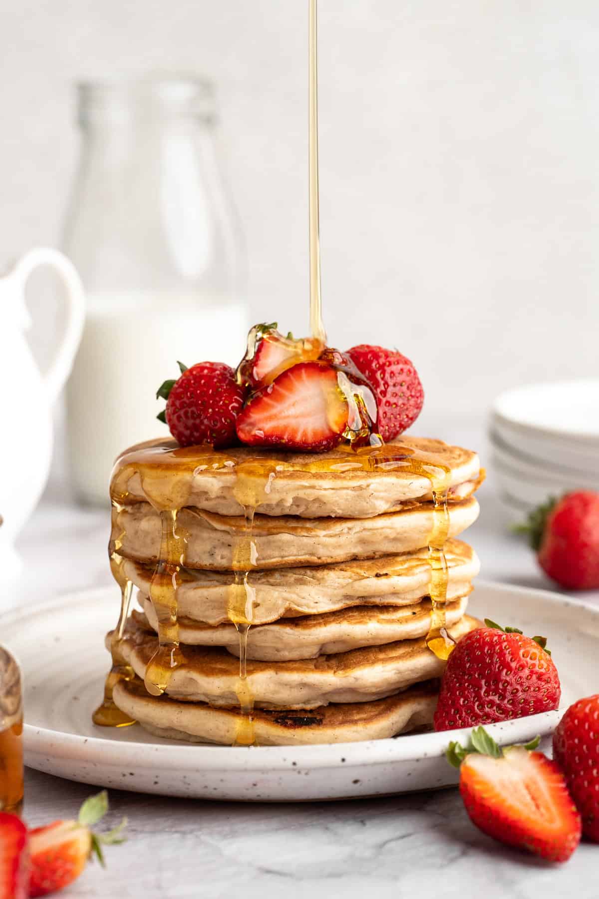 These strawberry pancakes are incredibly fluffy and jam-packed with fresh strawberries. Plus, they're gluten-free and vegan! Drizzling maple syrup over a stack of strawberry pancakes.