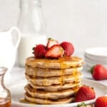 A stack of gluten-free strawberry pancakes topped with fresh strawberries and maple syrup.