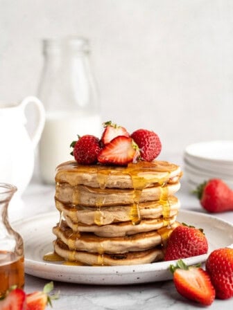 A stack of gluten-free strawberry pancakes topped with fresh strawberries and maple syrup.