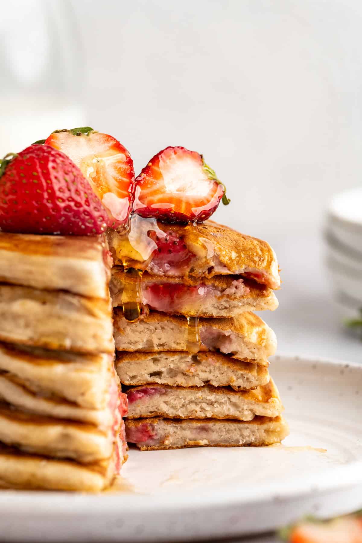 These strawberry pancakes are incredibly fluffy and jam-packed with fresh strawberries. Plus, they're gluten-free and vegan! A stack of strawberry pancakes with a big hunk cut out.