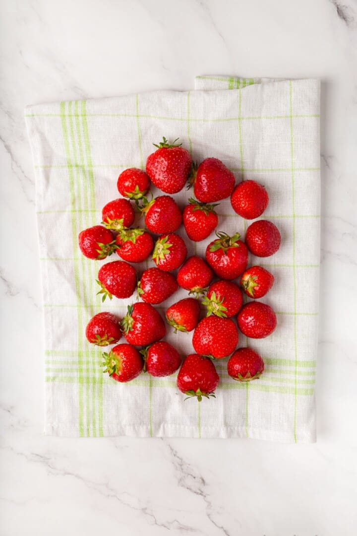 These beautifully simple macerated strawberries are so sweet and syrupy. They're a perfect addition to the breakfast OR dessert table. Whole strawberries on a dish towel.