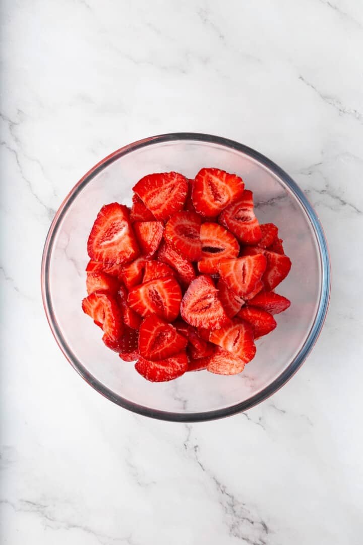 These beautifully simple macerated strawberries are so sweet and syrupy. They're a perfect addition to the breakfast OR dessert table. Hulled and sliced strawberries in a bowl.
