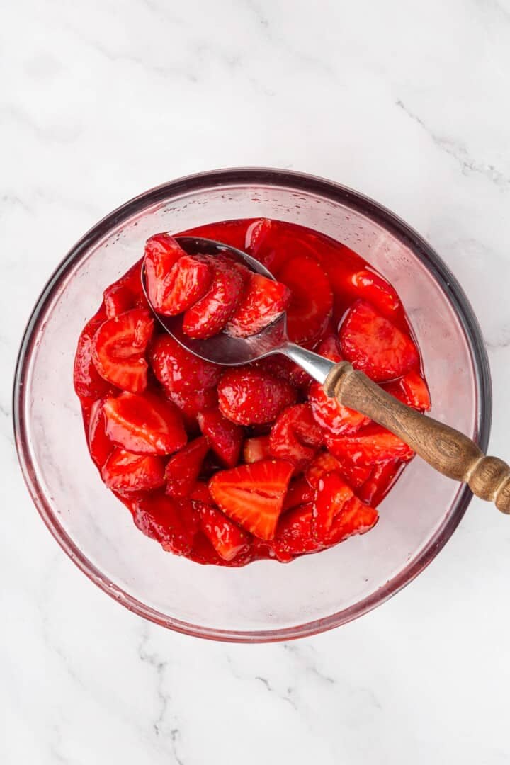 These beautifully simple macerated strawberries are so sweet and syrupy. They're a perfect addition to the breakfast OR dessert table. A glass bowl of strawberries that have been macerated.