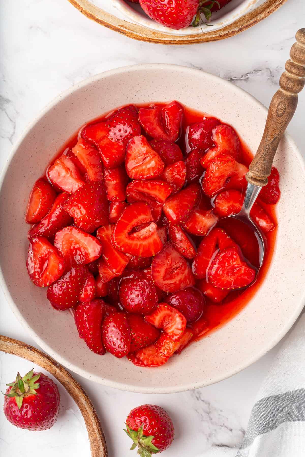 These beautifully simple macerated strawberries are so sweet and syrupy. They're a perfect addition to the breakfast OR dessert table. Overhead image of a bowl of syrupy macerated strawberries with a spoon in it.