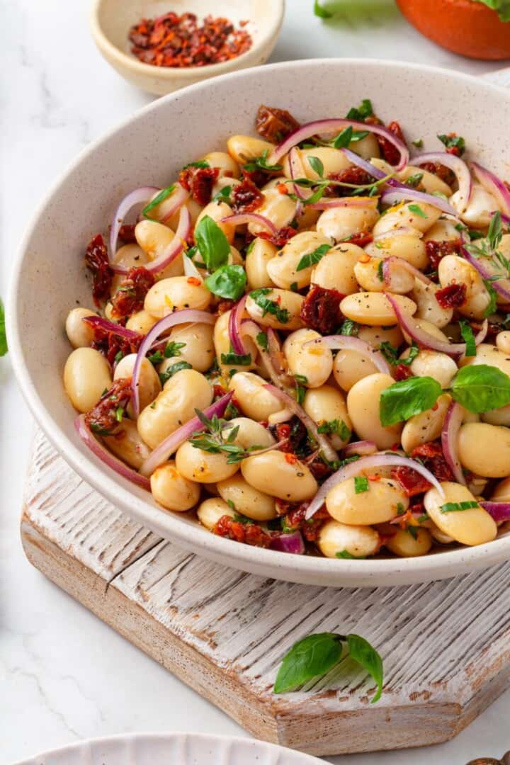 These easy marinated beans are soaked in a bright lemon-Dijon marinade with fresh herbs and aromatics. The perfect summer side. Tuscan-style marinated white beans in a serving bowl.