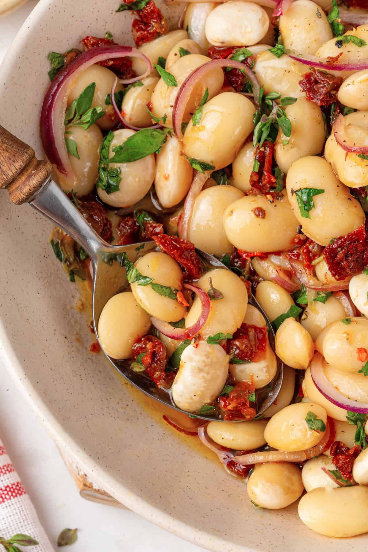 These easy marinated beans are soaked in a bright lemon-Dijon marinade with fresh herbs and aromatics. The perfect summer side. Overhead image of a bowl of marinated beans with a spoon in it.