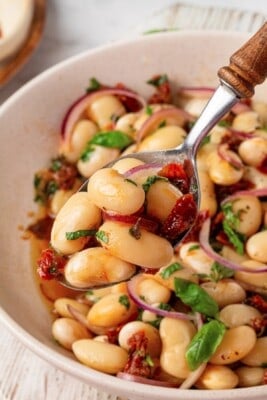 A spoon holding a bite of marinated beans up to the camera.