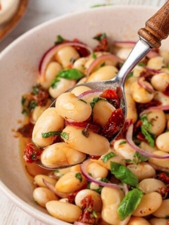 A spoon holding a bite of marinated beans up to the camera.