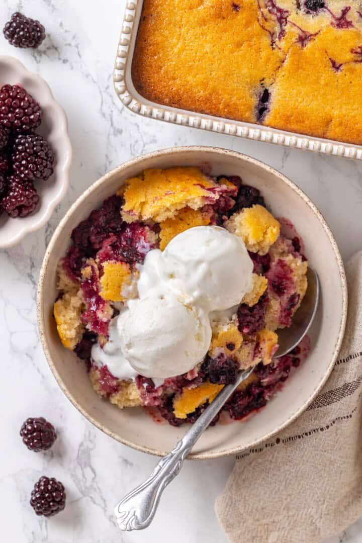 This blackberry cobbler, with its fluffy batter topping and juicy, bubbling blackberries is a summer staple you don't want to miss. Overhead image of blackberry cobbler in a bowl.