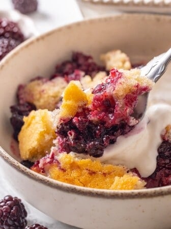 Close-up image of a spoon scooping up a bite of blackberry cobbler.