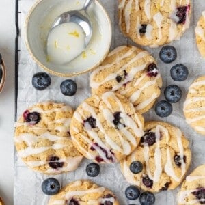 Vegan blueberry cookies on a cooling rack with a bowl of lemon glaze.