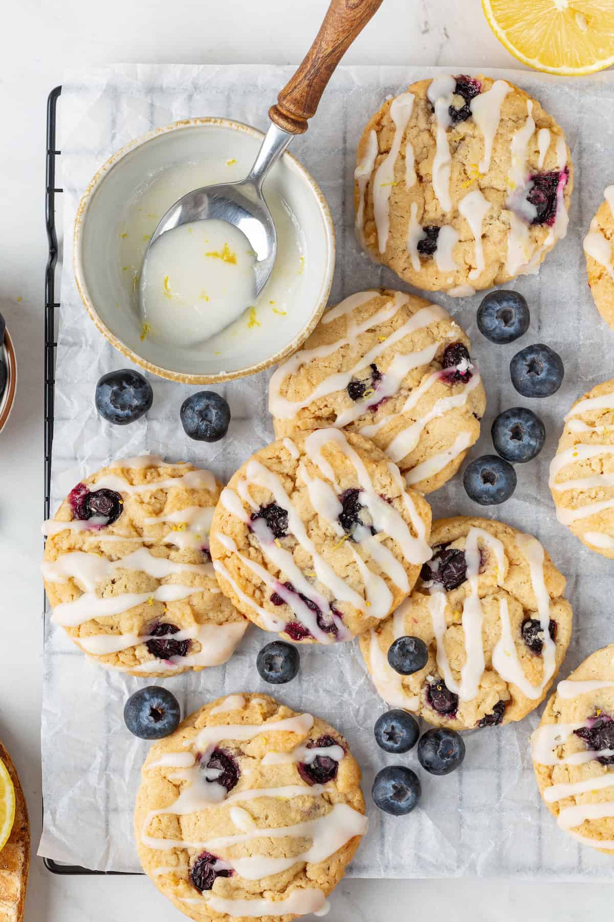 Loaded with jammy pockets of fresh berries and topped with a sweet lemon glaze, these vegan blueberry cookies are a summer must. Vegan blueberry cookies on a cooling rack with a bowl of lemon glaze.