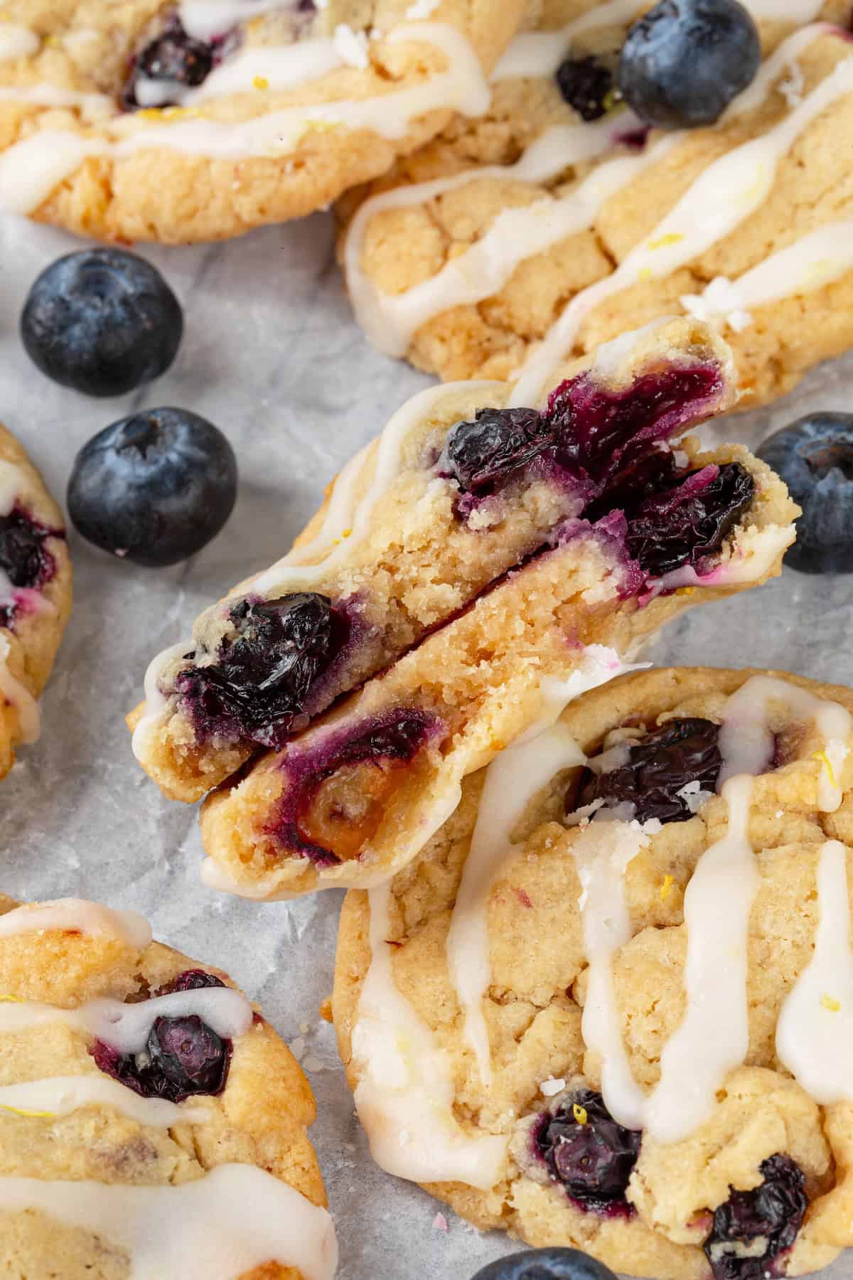 Loaded with jammy pockets of fresh berries and topped with a sweet lemon glaze, these vegan blueberry cookies are a summer must. Close-up of a lemon blueberry cookie broken in half to reveal the centre.