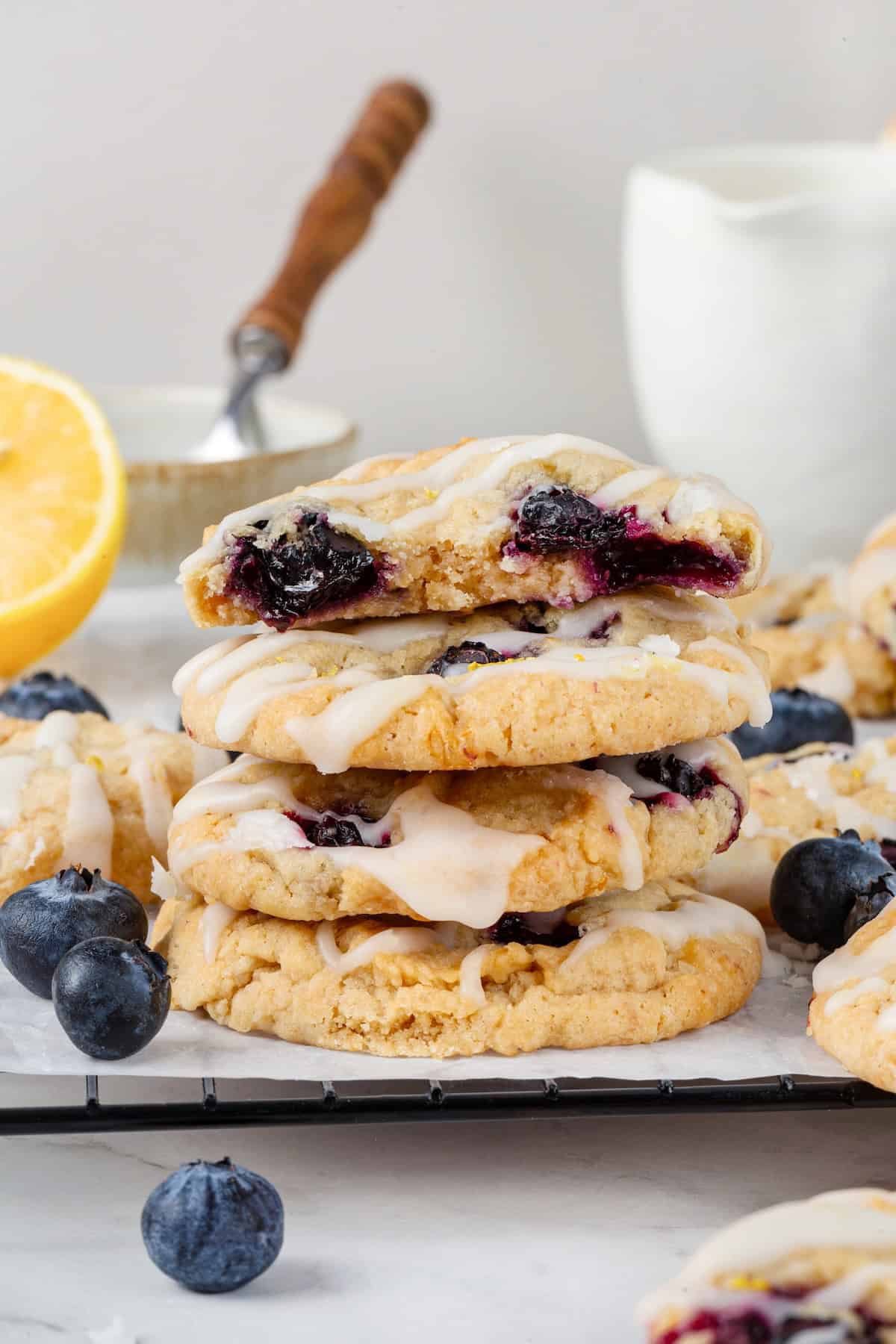 Loaded with jammy pockets of fresh berries and topped with a sweet lemon glaze, these vegan blueberry cookies are a summer must. A stack of blueberry lemon cookies. The top cookie is broken in half to reveal the inside.