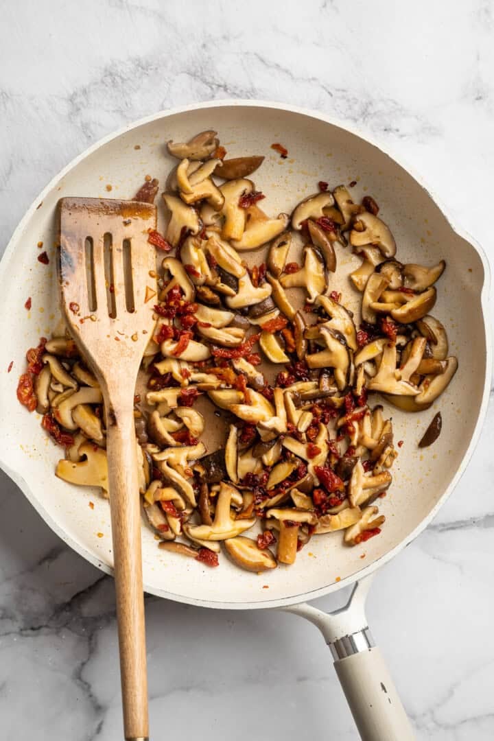 Saucy and loaded with veggies, this vegan cheesy pasta bake is topped with bubbly, melty vegan cheese. It's the ideal weeknight comfort food. Sautéing mushrooms, sun-dried tomatoes, and garlic in a skillet.