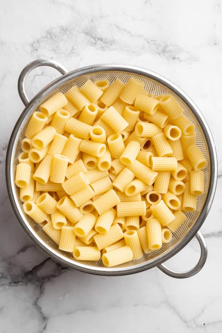 Saucy and loaded with veggies, this vegan cheesy pasta bake is topped with bubbly, melty vegan cheese. It's the ideal weeknight comfort food. Cooked rigatoni pasta in a colander.