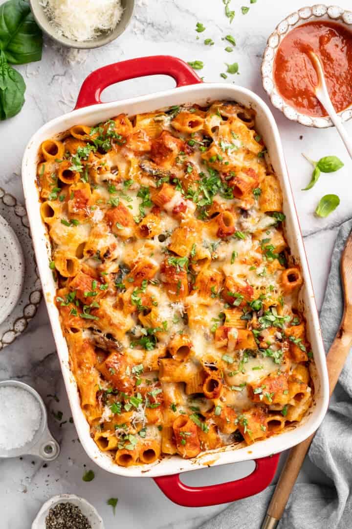 Saucy and loaded with veggies, this vegan cheesy pasta bake is topped with bubbly, melty vegan cheese. It's the ideal weeknight comfort food. Baked vegan cheesy pasta in a casserole dish.
