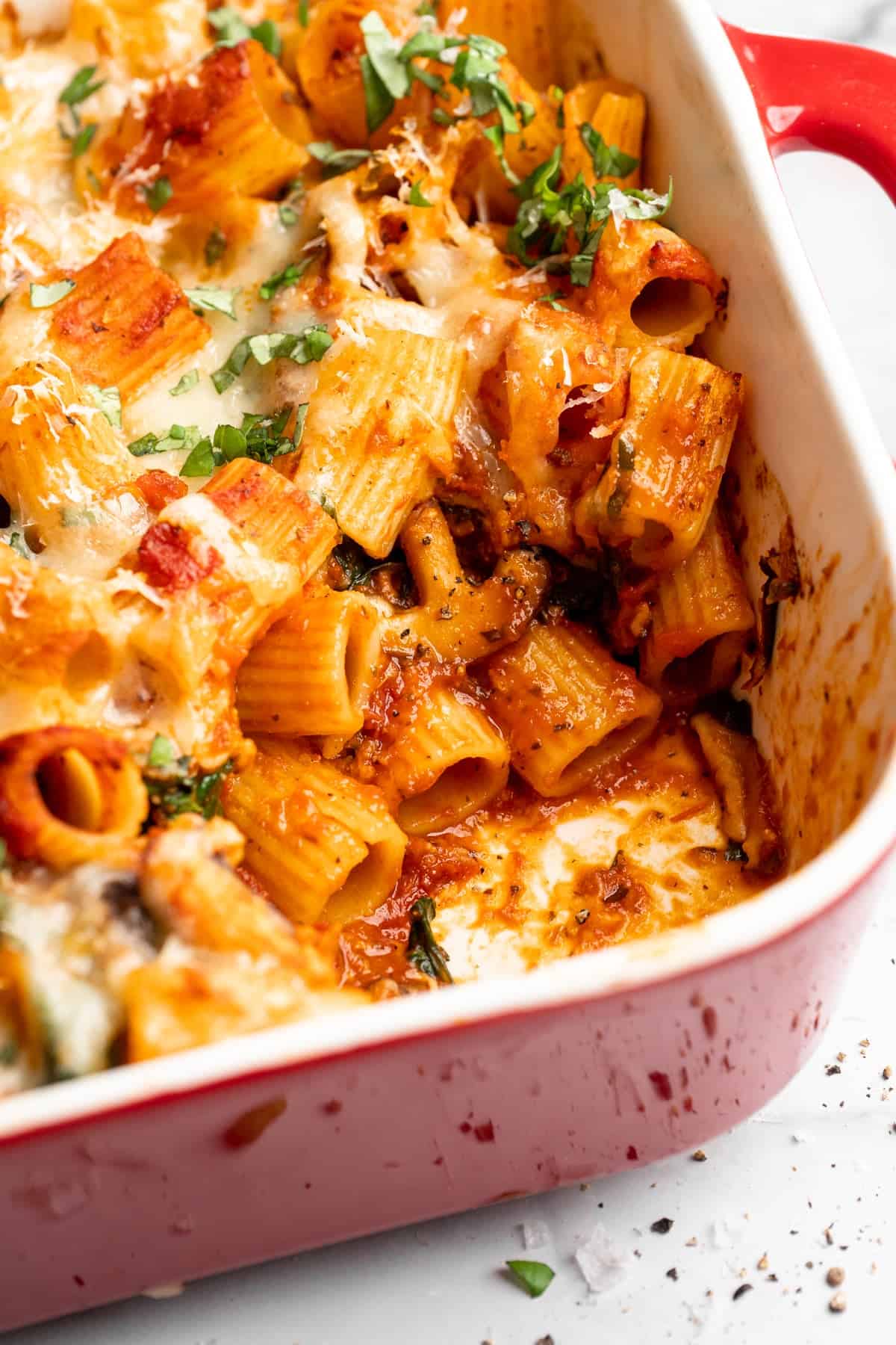 Saucy and loaded with veggies, this vegan cheesy pasta bake is topped with bubbly, melty vegan cheese. It's the ideal weeknight comfort food. Cheesy vegan pasta bake with a serving scooped out of the corner.