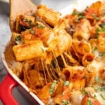 A wooden spatula scooping up a serving of baked vegan cheesy pasta.