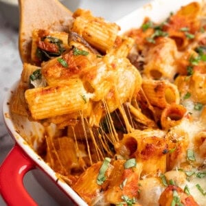 A wooden spatula scooping up a serving of baked vegan cheesy pasta.