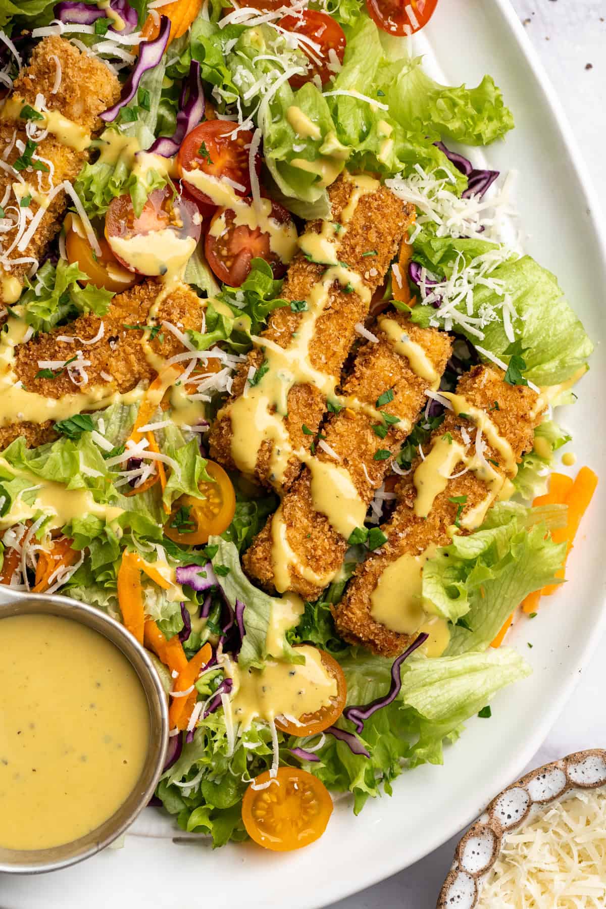 This tofu salad, topped with Cajun fried tofu and creamy, tangy-sweet dressing, is just as good as TGI Friday's version. And it's vegan! Close-up of Cajun fried tofu salad on a plate with extra dressing.