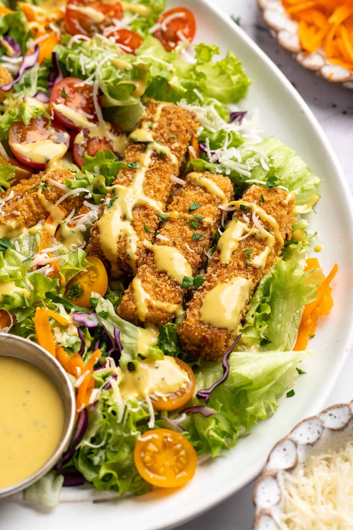 This tofu salad, topped with Cajun fried tofu and creamy, tangy-sweet dressing, is just as good as TGI Friday's version. And it's vegan! Cajun fried tofu salad on a plate with a little extra dressing on the side.
