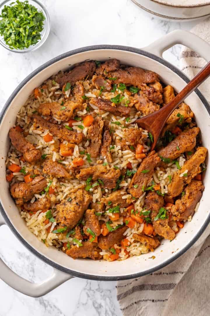 This vegan "chicken" and rice delivers all the cozy, savoury goodness of the meat-eater's version, no chicken required. Adding parsley to vegan chicken and rice fresh out of the oven.