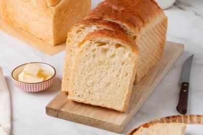 A loaf of sandwich bread with two slices leaning against it.