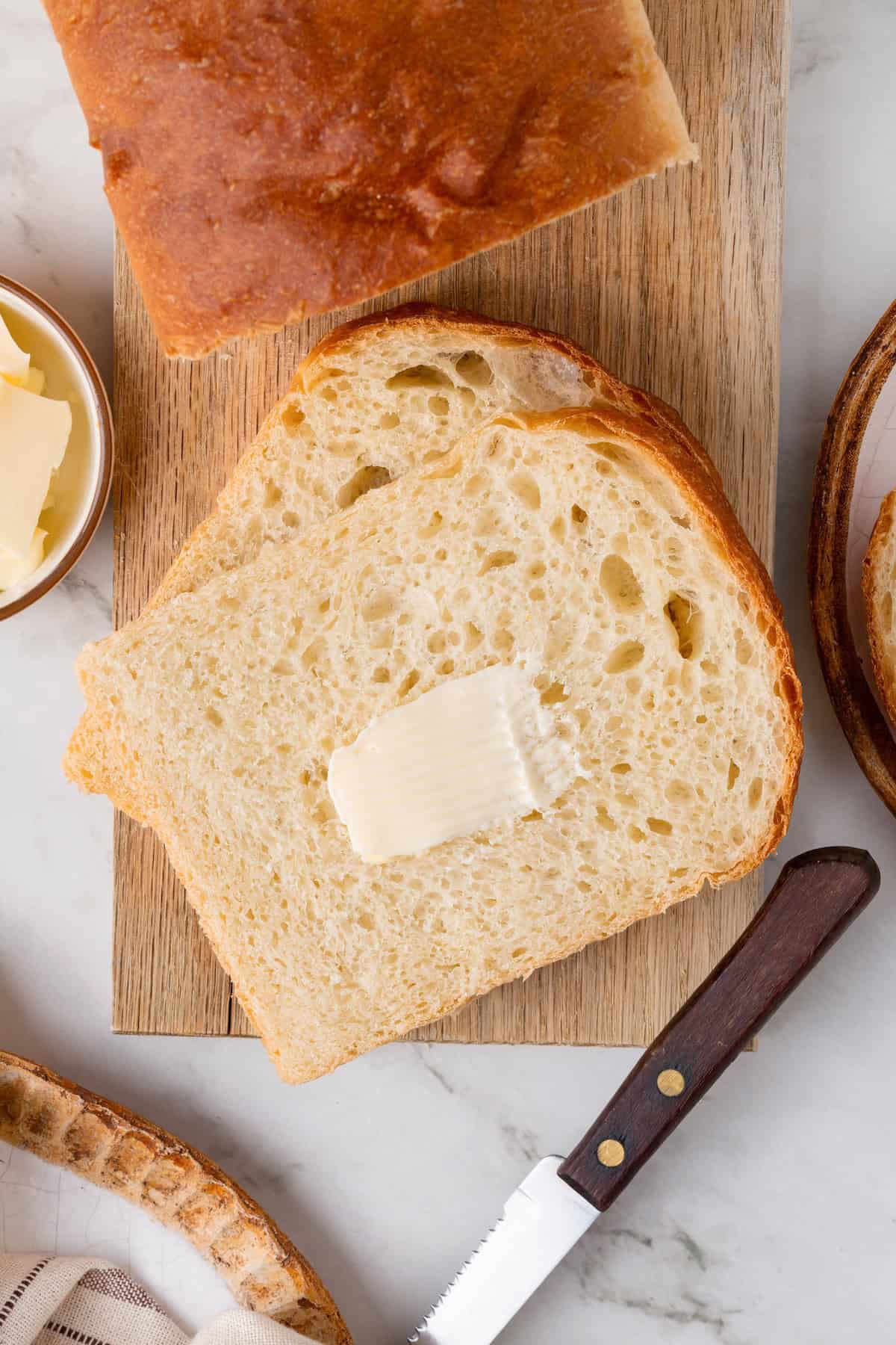 This easy vegan Sandwich Bread Recipe is a home baker's dream. Soft and pillowy with a subtle richness, it's a major upgrade to any sandwich. Overhead image of slices of homemade sandwich bread. One has butter smeared on it.