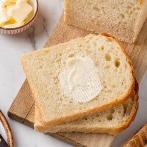 Slices of homemade sandwich bread. One has butter smeared on it.