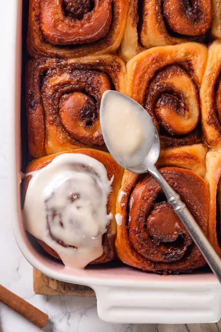 These vegan sourdough cinnamon rolls are impossibly soft, packed with cinnamon sugar filling, and topped with a smooth cream cheese glaze. Overhead image of spooning cream cheese glaze over vegan sourdough cinnamon rolls.