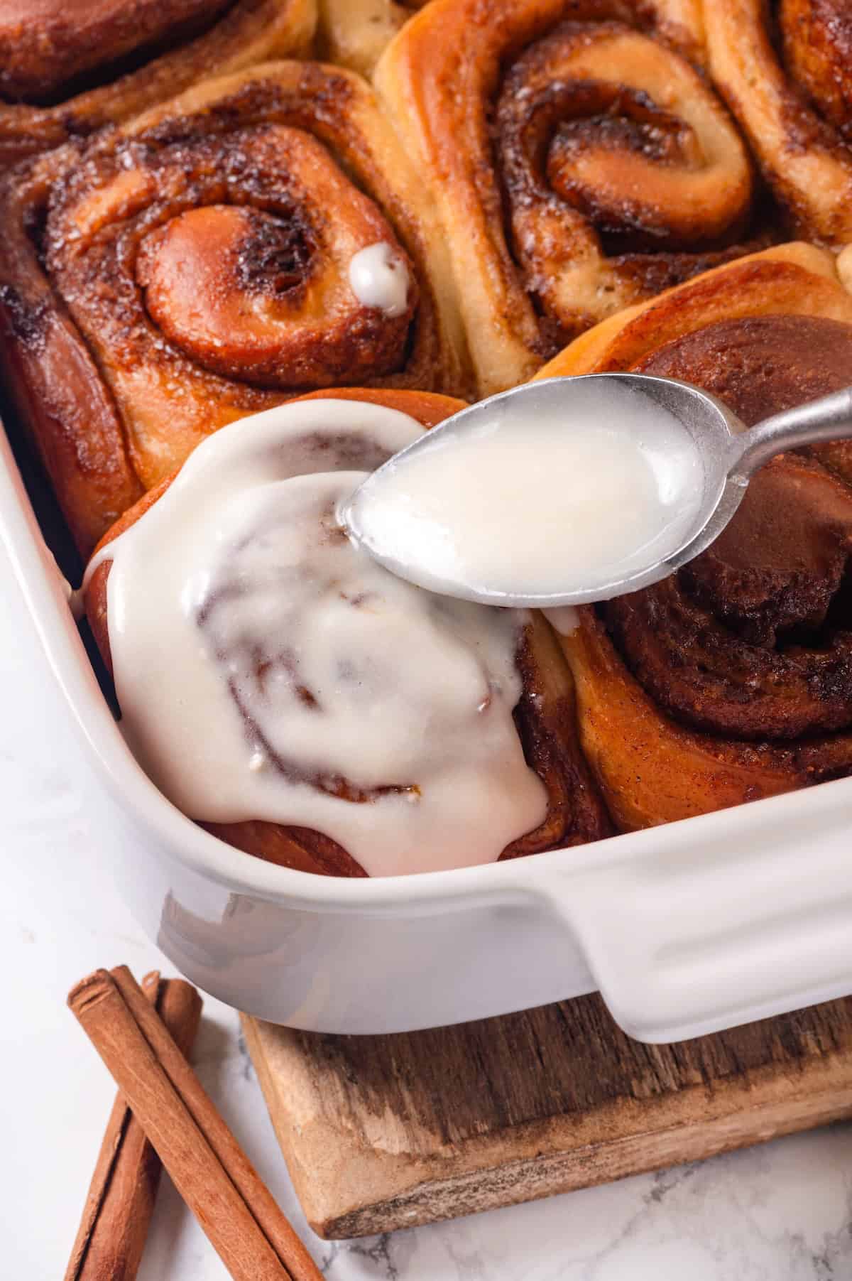 These vegan sourdough cinnamon rolls are impossibly soft, packed with cinnamon sugar filling, and topped with a smooth cream cheese glaze. Spooning cream cheese glaze over vegan sourdough cinnamon rolls.