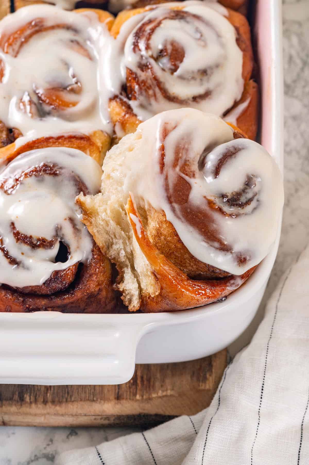 These vegan sourdough cinnamon rolls are impossibly soft, packed with cinnamon sugar filling, and topped with a smooth cream cheese glaze. A vegan sourdough cinnamon roll pulled slightly out of the pan.