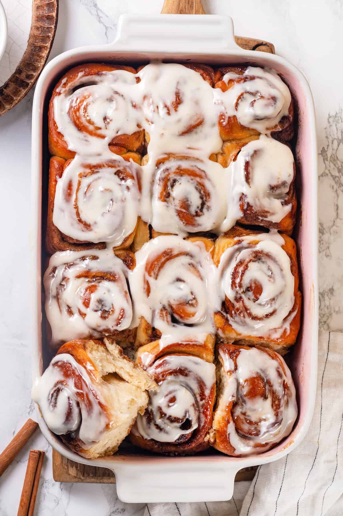 These vegan sourdough cinnamon rolls are impossibly soft, packed with cinnamon sugar filling, and topped with a smooth cream cheese glaze. A pan of vegan sourdough cinnamon rolls. The left corner roll is pulled out slightly.