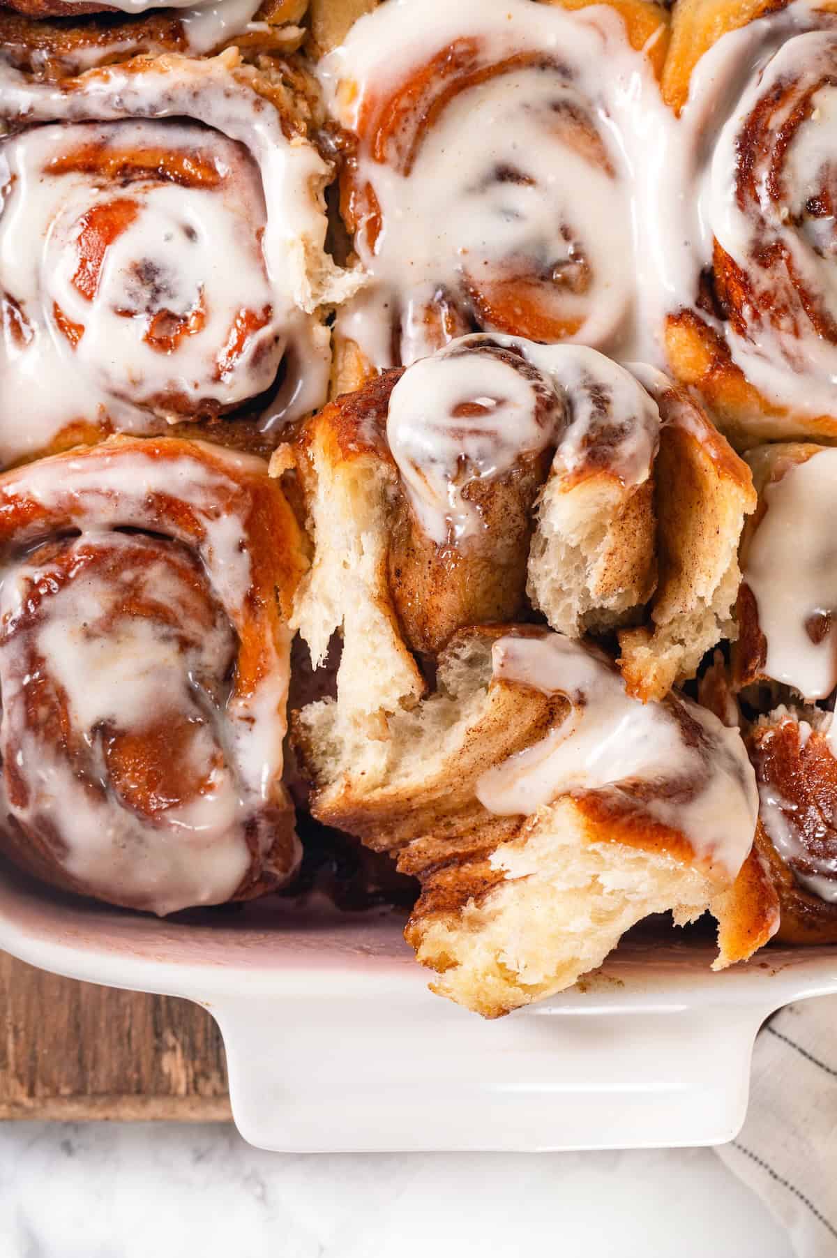 These vegan sourdough cinnamon rolls are impossibly soft, packed with cinnamon sugar filling, and topped with a smooth cream cheese glaze. Close-up image of a cinnamon roll pulled out of the pan and pulled apart a bit to reveal the soft, tender center.