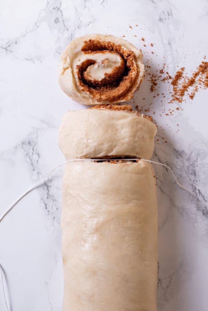 These vegan sourdough cinnamon rolls are impossibly soft, packed with cinnamon sugar filling, and topped with a smooth cream cheese glaze. Dough filled with butter, cinnamon, and sugar and rolled into a log being cut into rolls.