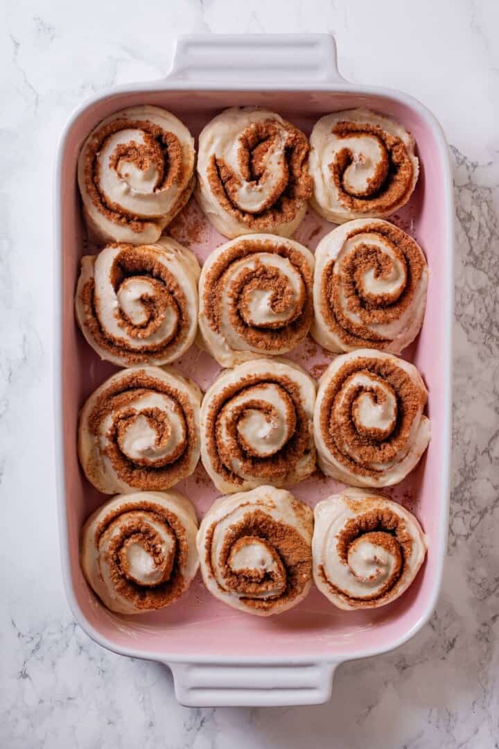 These vegan sourdough cinnamon rolls are impossibly soft, packed with cinnamon sugar filling, and topped with a smooth cream cheese glaze. Unbaked cinnamon rolls arranged in a baking pan.