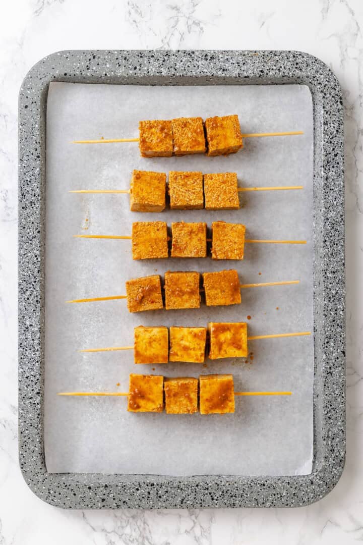 Move over, chicken satay. This tofu satay delivers all the sweet, savoury, tang you crave, with firm caramelised tofu and Thai peanut sauce. Marinated tofu threaded onto skewers and arranged on a baking sheet.