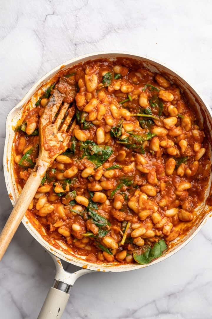 These 30-minute smoky white beans in tomato sauce are made with liquid smoke and plenty of garlic. They're amazing on toast for breakfast! Stirring spinach into smoky white beans in garlicky tomato sauce.