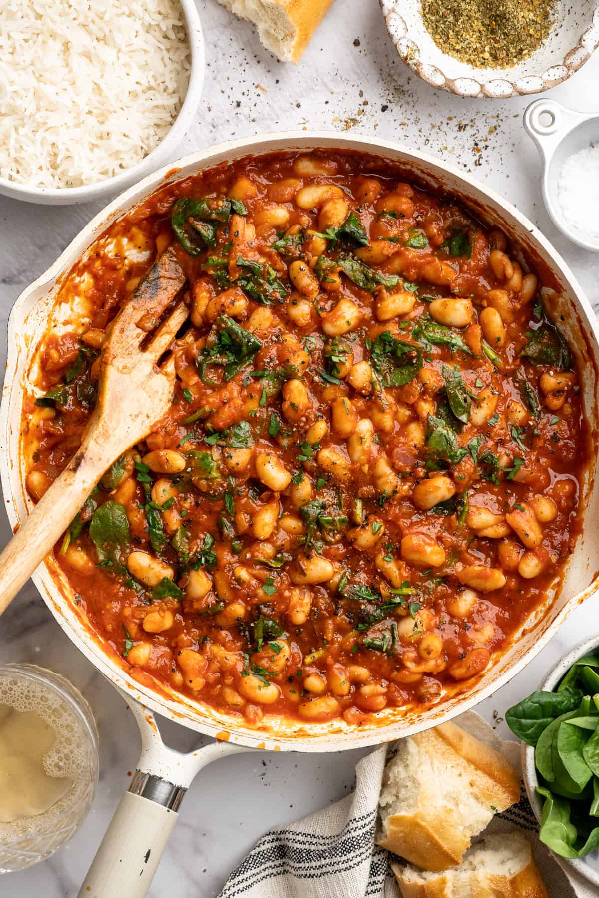 These 30-minute smoky white beans in tomato sauce are made with liquid smoke and plenty of garlic. They're amazing on toast for breakfast! Overhead image of smoky white beans in tomato sauce in a skillet with a wooden spatula.